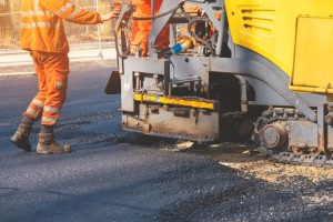 A stock photo of a worker in high vis PPE handling a machine involved with surfacing a road